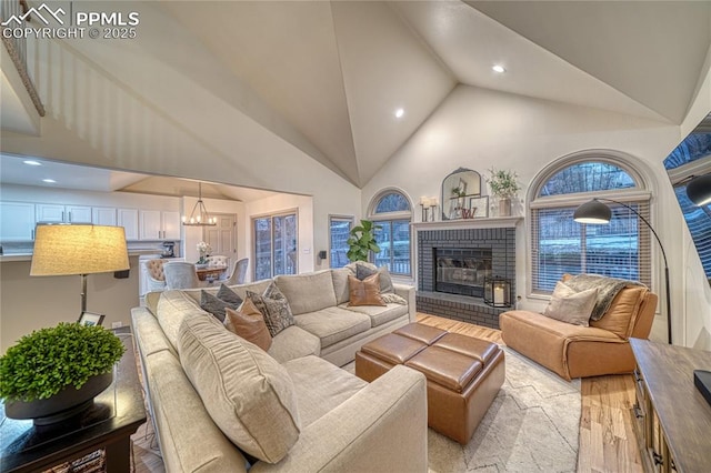 living room featuring high vaulted ceiling, a notable chandelier, a fireplace, and light hardwood / wood-style flooring