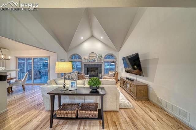 living room with a brick fireplace, high vaulted ceiling, a notable chandelier, and light hardwood / wood-style floors