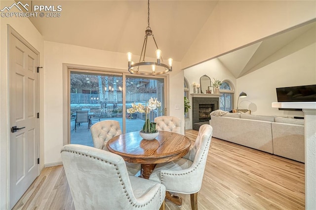 dining room with lofted ceiling, a brick fireplace, light hardwood / wood-style flooring, and a chandelier