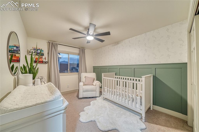 bedroom with a crib, ceiling fan, and carpet flooring