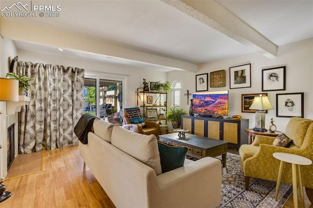 living area with beamed ceiling, a fireplace, and wood finished floors