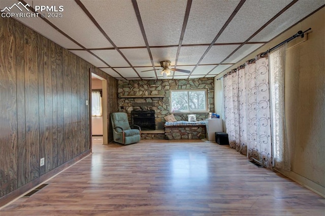 unfurnished room featuring hardwood / wood-style floors, a fireplace, ceiling fan, and wood walls