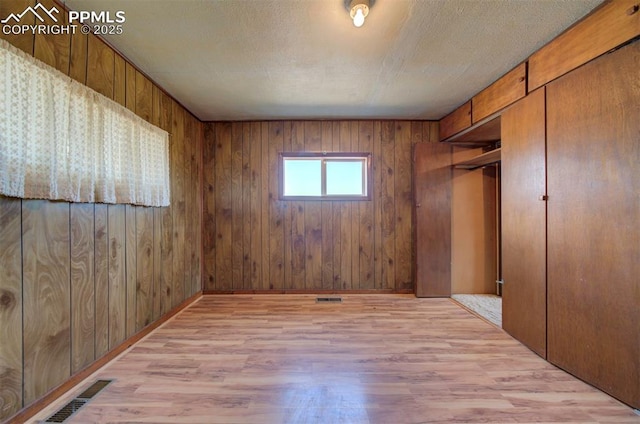 interior space featuring wooden walls, a textured ceiling, and light wood-type flooring