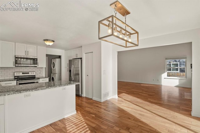 kitchen featuring decorative light fixtures, white cabinets, dark stone counters, stacked washer / drying machine, and stainless steel appliances