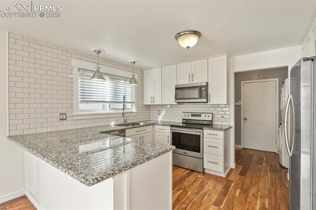 kitchen featuring stainless steel appliances, kitchen peninsula, stone countertops, and white cabinets