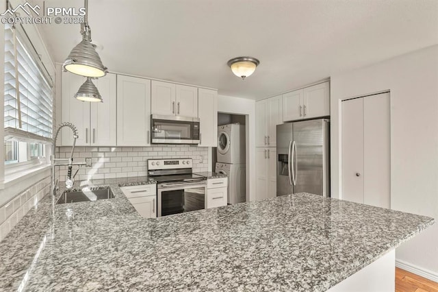 kitchen with stacked washer and dryer, sink, white cabinetry, appliances with stainless steel finishes, and kitchen peninsula