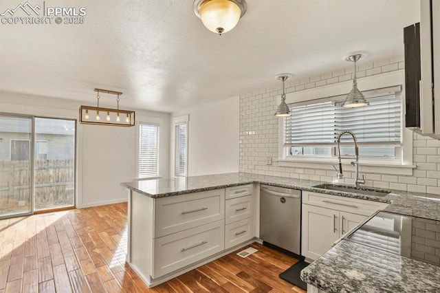 kitchen with sink, hanging light fixtures, kitchen peninsula, dishwasher, and white cabinets