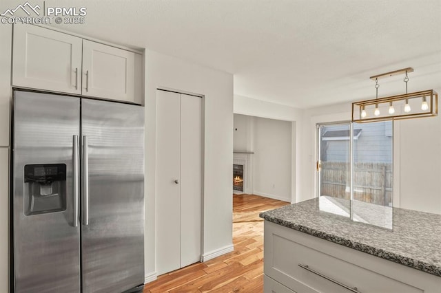 kitchen with pendant lighting, stainless steel fridge, stone counters, light hardwood / wood-style floors, and white cabinets