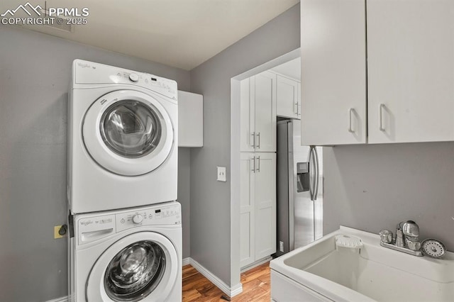 washroom featuring cabinets, stacked washer and clothes dryer, sink, and light hardwood / wood-style flooring