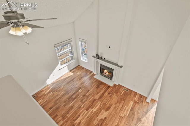 unfurnished living room featuring ceiling fan, vaulted ceiling, light hardwood / wood-style flooring, and a textured ceiling