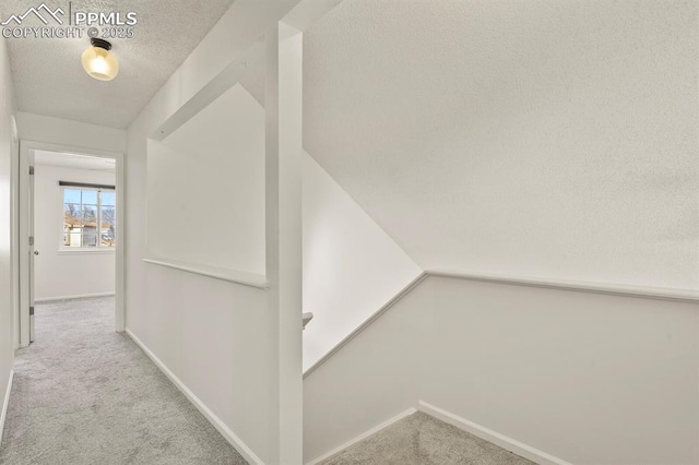 hallway featuring light colored carpet and a textured ceiling