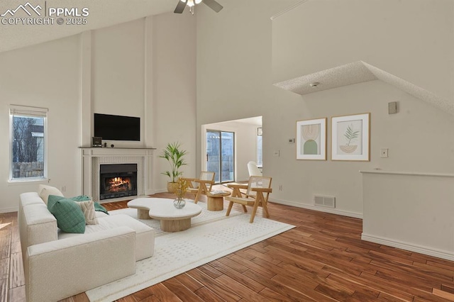 living room with a tiled fireplace, wood-type flooring, ceiling fan, and plenty of natural light