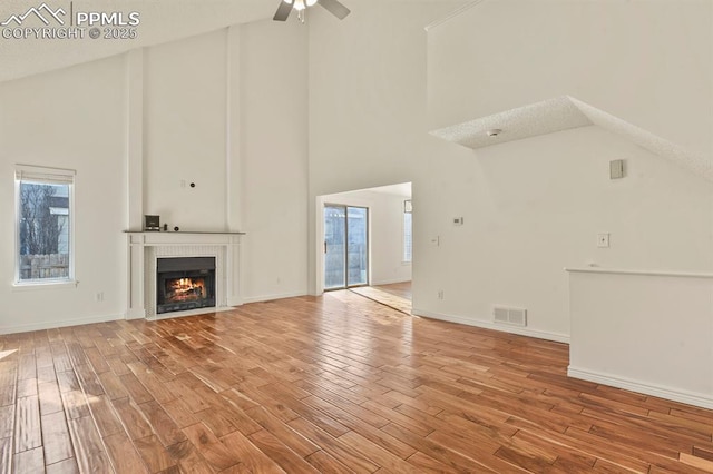 unfurnished living room with ceiling fan, high vaulted ceiling, and light hardwood / wood-style floors