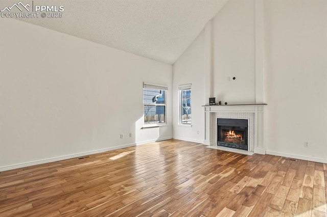 unfurnished living room featuring hardwood / wood-style floors, a fireplace, high vaulted ceiling, and a textured ceiling