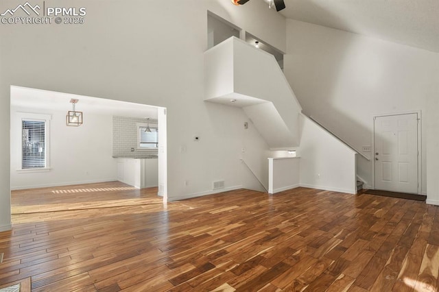 unfurnished living room with wood-type flooring, ceiling fan, and high vaulted ceiling