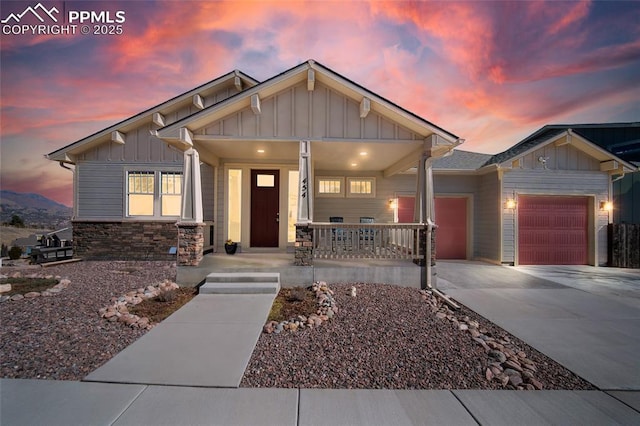 craftsman-style house featuring covered porch, an attached garage, board and batten siding, stone siding, and driveway