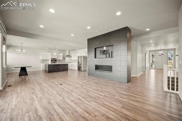 unfurnished living room with light wood finished floors, recessed lighting, a large fireplace, a chandelier, and baseboards