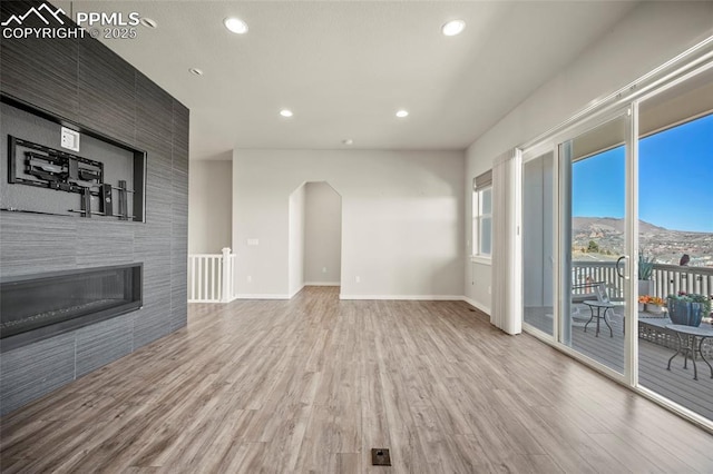 unfurnished living room featuring baseboards, arched walkways, a tile fireplace, wood finished floors, and recessed lighting