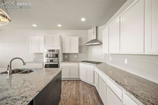 kitchen with light wood-style flooring, appliances with stainless steel finishes, white cabinets, a sink, and wall chimney range hood