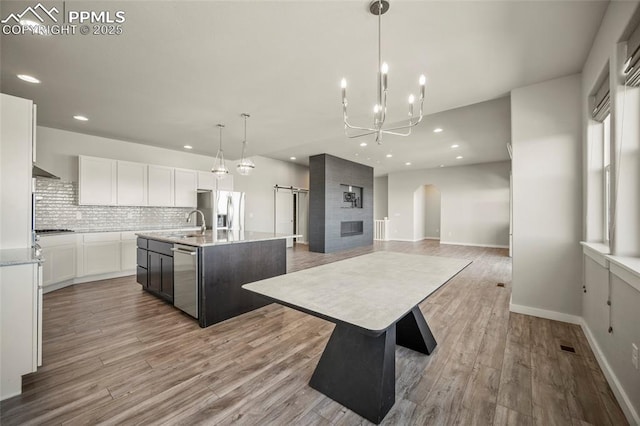 kitchen featuring a kitchen island with sink, white cabinets, appliances with stainless steel finishes, light wood-type flooring, and decorative backsplash