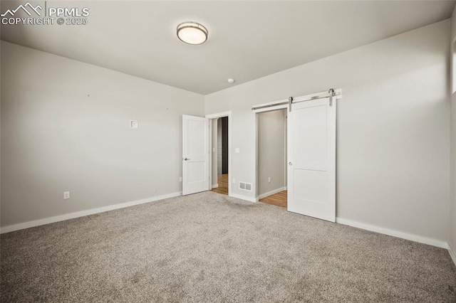 unfurnished bedroom with baseboards, a barn door, visible vents, and carpet flooring