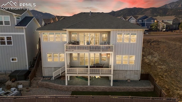 back of property at dusk with a shingled roof, a mountain view, and a balcony