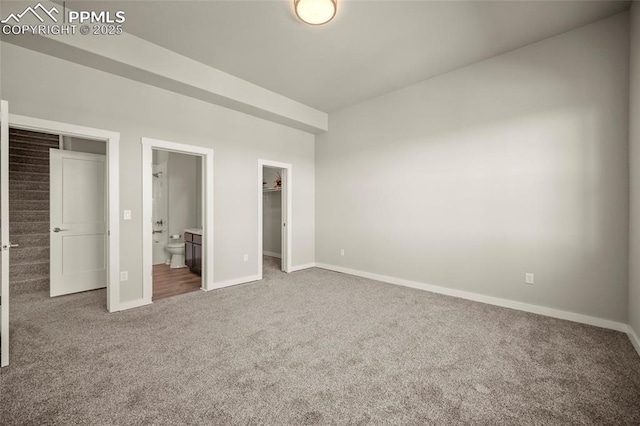 unfurnished bedroom featuring ensuite bathroom, carpet floors, a spacious closet, and baseboards