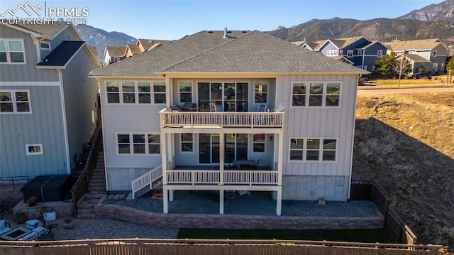 back of house featuring a shingled roof, a mountain view, a balcony, and stairs