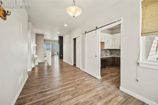 corridor featuring light wood-type flooring, baseboards, an upstairs landing, and a barn door