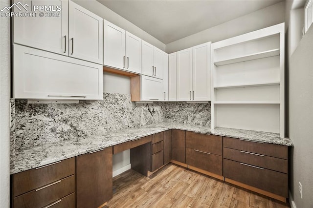 interior space featuring decorative backsplash, built in study area, light wood-type flooring, white cabinetry, and open shelves