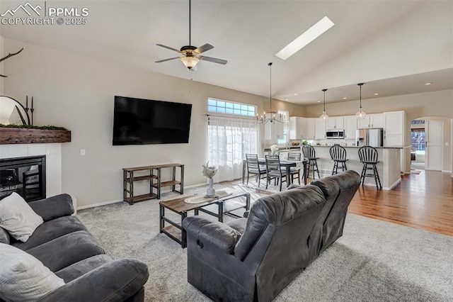 living room featuring ceiling fan with notable chandelier, a fireplace, high vaulted ceiling, and light hardwood / wood-style floors