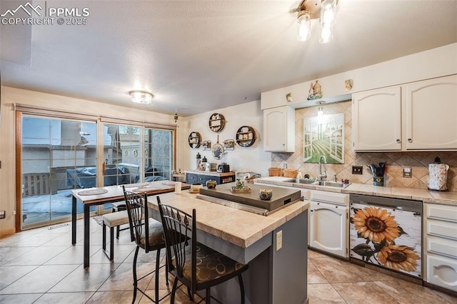 kitchen with light tile patterned flooring, sink, white cabinets, backsplash, and stainless steel dishwasher