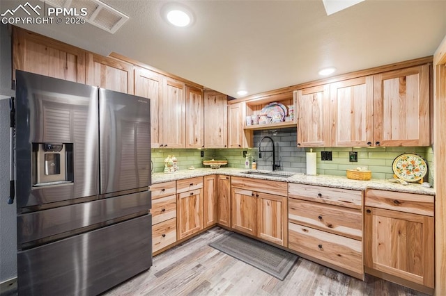 kitchen featuring sink, light hardwood / wood-style flooring, stainless steel fridge, backsplash, and light stone countertops