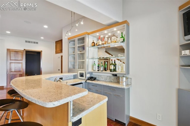 kitchen featuring gray cabinetry, a breakfast bar, a center island, light stone countertops, and pendant lighting