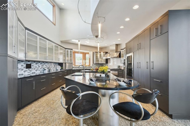 kitchen featuring sink, dark brown cabinetry, a kitchen island with sink, and wall chimney range hood