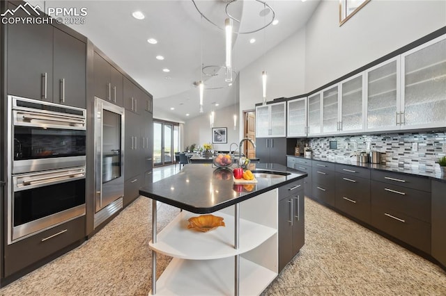 kitchen featuring a kitchen island with sink, a breakfast bar, sink, backsplash, and double oven