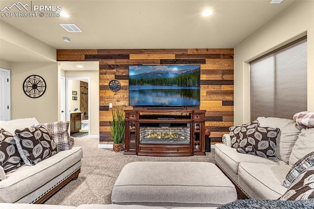 living area featuring recessed lighting, visible vents, carpet flooring, wood walls, and a warm lit fireplace