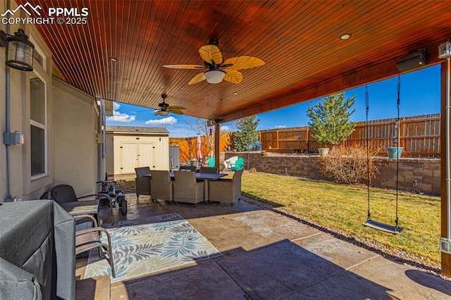 view of patio / terrace featuring an outbuilding, a fenced backyard, a ceiling fan, a shed, and outdoor dining space