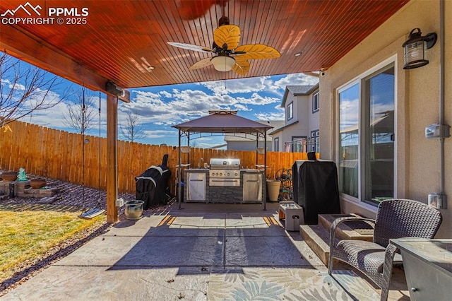 view of patio with an outdoor kitchen, a ceiling fan, a fenced backyard, a grill, and a gazebo