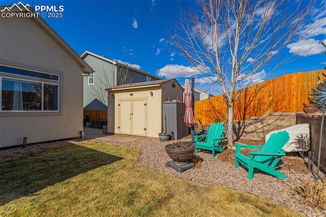 view of yard with an outdoor fire pit, a storage unit, a fenced backyard, and an outbuilding