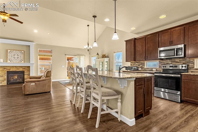 kitchen featuring light stone counters, a breakfast bar, decorative light fixtures, appliances with stainless steel finishes, and an island with sink