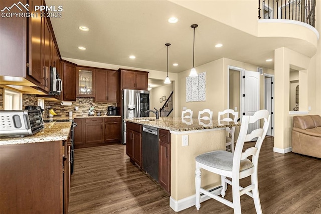 kitchen featuring a toaster, a center island with sink, appliances with stainless steel finishes, dark wood-style flooring, and decorative light fixtures