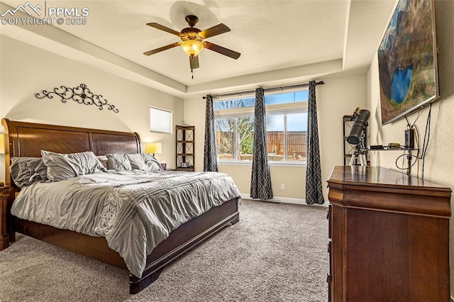 carpeted bedroom featuring ceiling fan, a raised ceiling, and baseboards