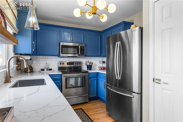 kitchen featuring appliances with stainless steel finishes, decorative light fixtures, sink, light stone countertops, and blue cabinetry