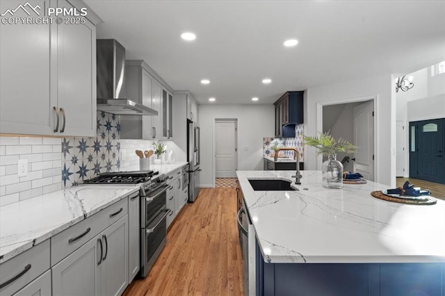 kitchen with sink, appliances with stainless steel finishes, light hardwood / wood-style floors, decorative backsplash, and wall chimney exhaust hood