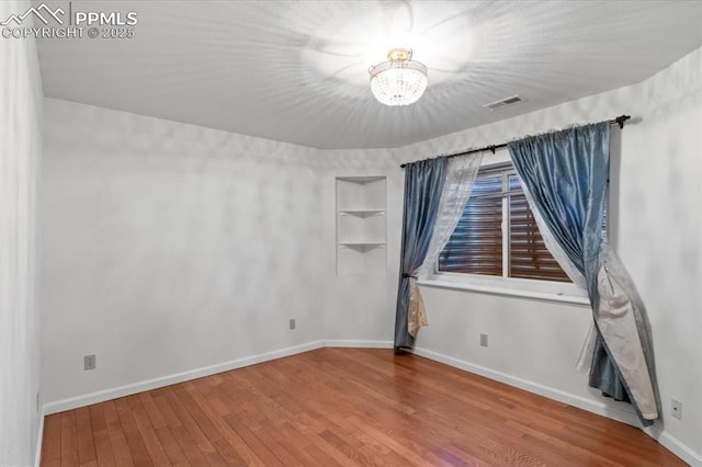 spare room with hardwood / wood-style flooring, a chandelier, and built in features