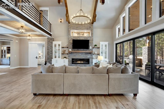 living room with a stone fireplace, high vaulted ceiling, light hardwood / wood-style flooring, and a notable chandelier