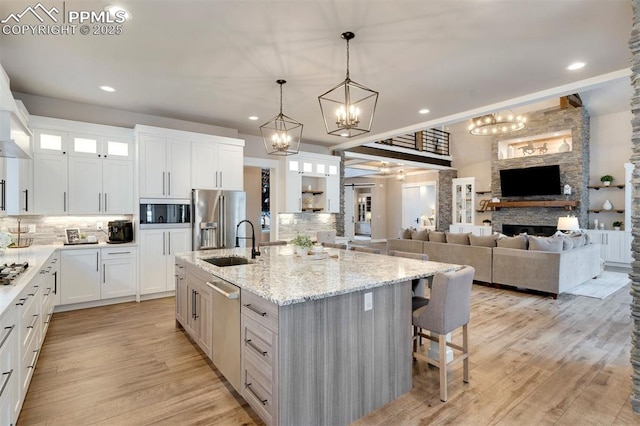 kitchen with sink, hanging light fixtures, appliances with stainless steel finishes, a kitchen island with sink, and white cabinets