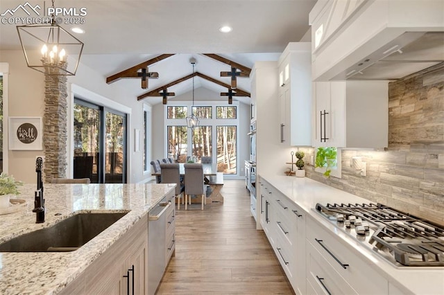 kitchen with sink, custom exhaust hood, white cabinetry, light stone counters, and hanging light fixtures