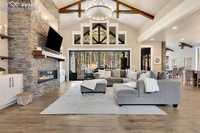 living room with an inviting chandelier, a stone fireplace, light hardwood / wood-style flooring, and a wealth of natural light